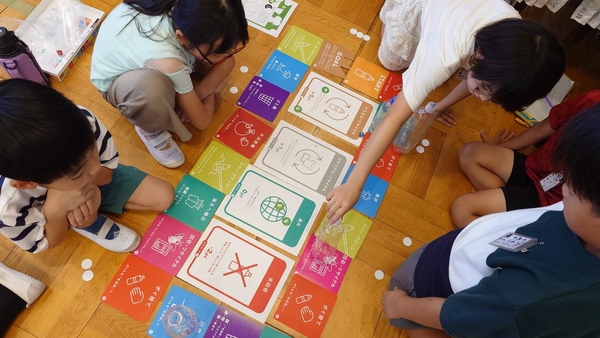 ペットボトル水平リサイクルを学べるすごろくである、リサイコロの周りを囲む生徒達